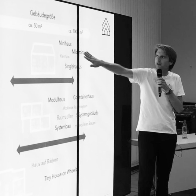 Das Bild zeigt den Tiny House Experten Christian Brecht bei einem Vortrag. Zu sehen ist der Referent und eine Powerpoint Präsentation über Tiny House Typen.