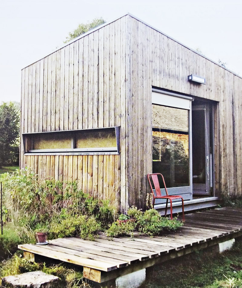 Das Bild zeigt ein Minihaus mit Holzfassade. Vor der dem Minihaus ist ein Holzterrasse.