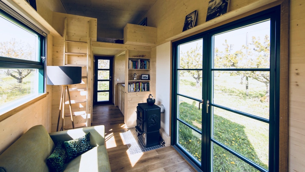 Das Bild zeigt die Innenansicht eines Haus auf Rädern. Man sieht in das Innenleben des Haus auf Rädern. Zu sehen ist ein Loft für den Schlafbereich, ein Sofa, ein Ofen und eine Lampe